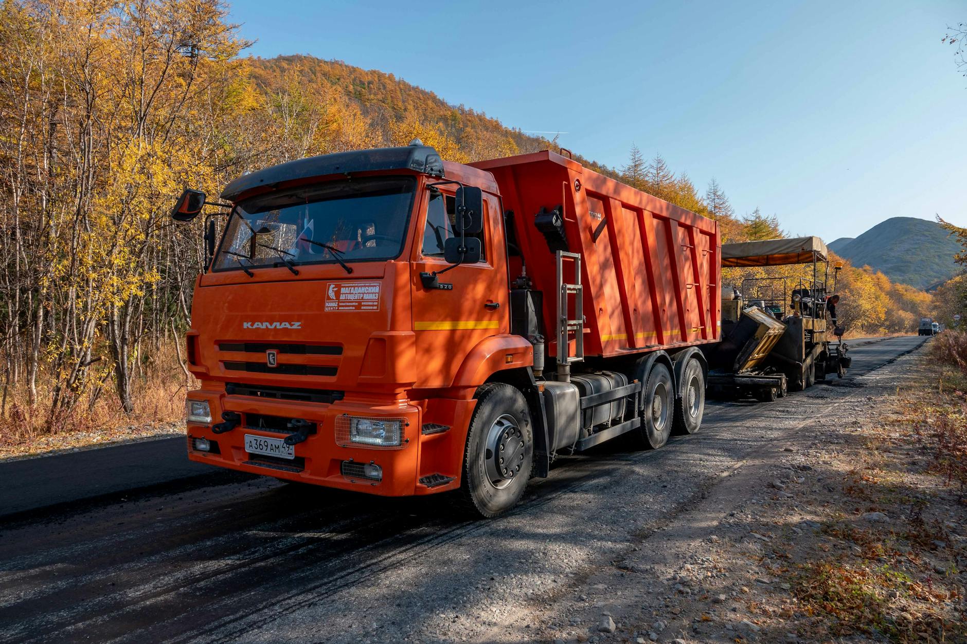 bright orange truck paving road in autumn forest
